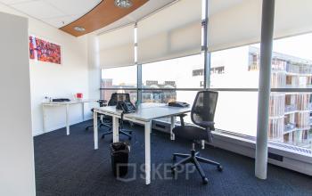 A bright office space at Avenue Ceramique 221, Maastricht, featuring several desks and chairs with natural light streaming in through large windows.