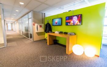 Bright hallway at Avenue Ceramique 221, Maastricht, ideal for office space rental, featuring vibrant green walls, modern lighting, and a wooden desk with printers, enhancing the appeal of this office to rent.