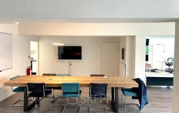Spacious office to rent at Wilhelminasingel 44-46, Maastricht featuring a long wooden table, chairs, and a wall-mounted screen suitable for meetings.