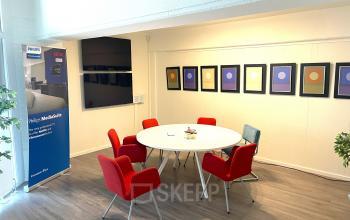 Bright office space at Wilhelminasingel 44-46, Maastricht, featuring a round table surrounded by vibrant red chairs, ideal for meetings or collaborative sessions.
