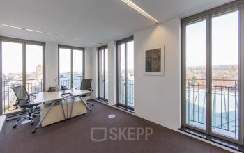 Bright office space rental at Stationsplein 8K, Maastricht, with a desk, chairs, and large windows offering a city view.