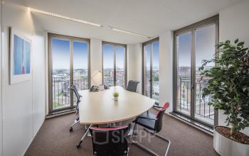 Modern office space rental at Stationsplein 8K, Maastricht with a large window offering a bright view, complete with a smart meeting table setup.
