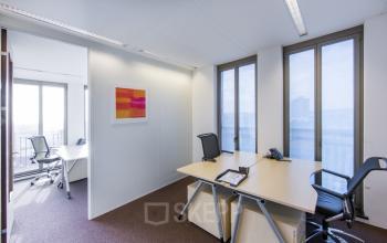 Modern office space rental at Stationsplein 8K, Maastricht, featuring a well-lit room with desks, chairs, and a vibrant painting.
