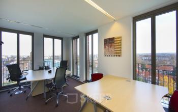 Modern office space rental at Stationsplein 8K, Maastricht, featuring a large table, chairs, and ample natural light with a city view.