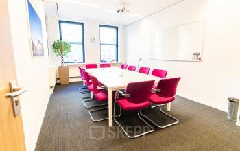 Bright conference room with a long table and vibrant red chairs, suitable for office space rental at Robert Schumandomein 2, Maastricht.