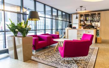 Bright office reception area at Robert Schumandomein 2 in Maastricht, featuring vibrant magenta chairs, modern decor, and a welcoming receptionist at the desk. Perfect office space rental option.