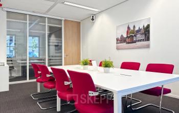 Bright office space at Robert Schumandomein 2, Maastricht, featuring a meeting table with vibrant red chairs and potted plants, ideal for office space rental.