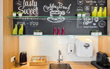 A stylish pantry area in an office to rent at Robert Schumandomein 2, Maastricht, featuring a sink, coffee machine, and decorative chalkboard walls with vibrant accents.