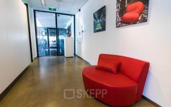 Spacious office entrance at Brieltjenspolder 28, Made, featuring a vibrant red couch and art on the walls, ideal for office space rental.