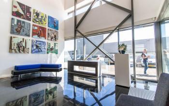 Bright office entrance with modern art on the wall, glass windows, and seating area. A person is walking outside. Ideal for office space rental.