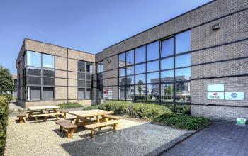 Exterior view of office building at Generaal de Wittelaan 11a, Mechelen North, with outdoor seating area and modern glass windows, ideal for office space rental.