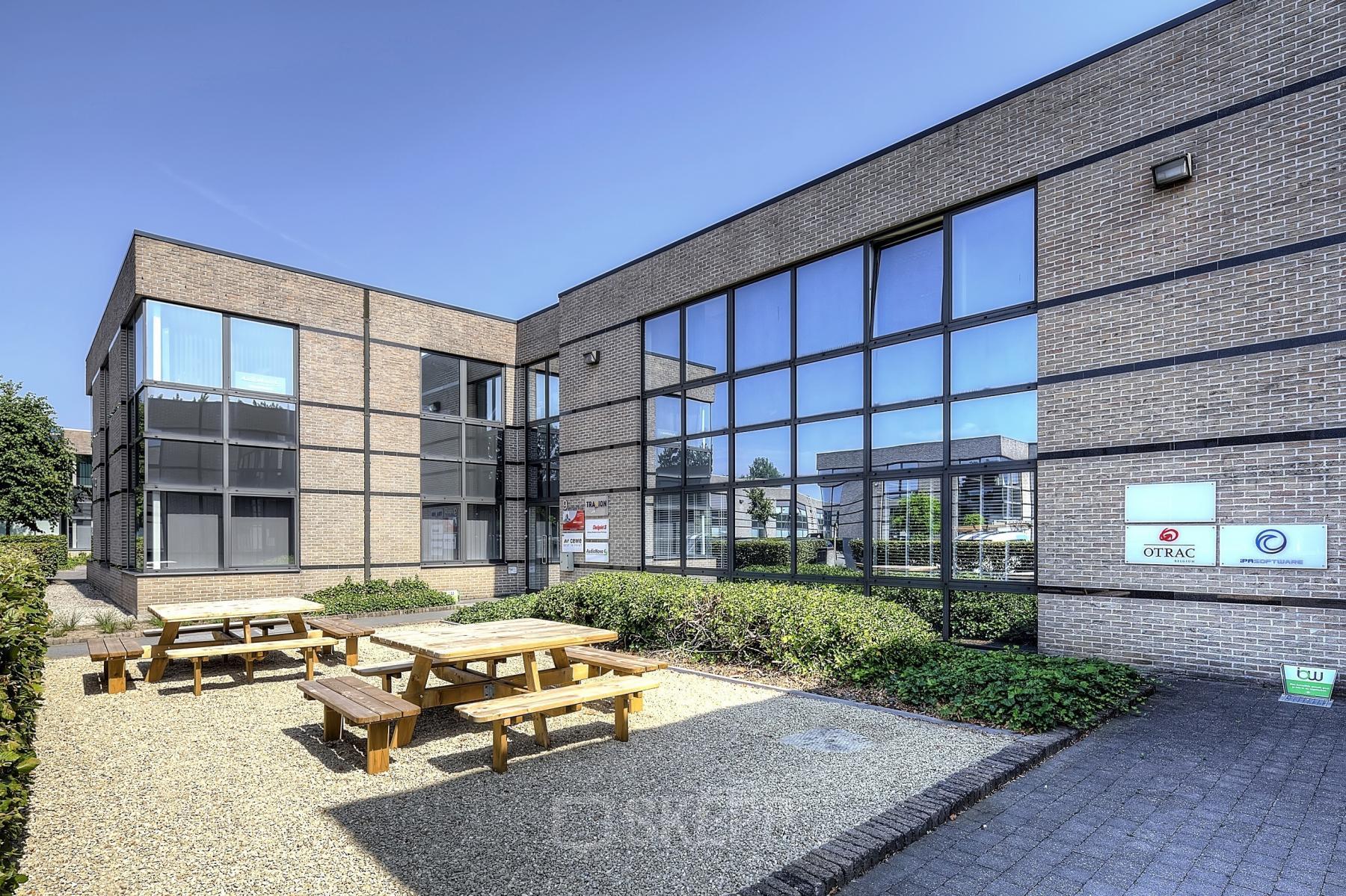 Exterior view of office building at Generaal de Wittelaan 11a, Mechelen North, with outdoor seating area and modern glass windows, ideal for office space rental.