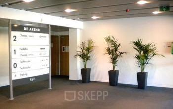 Entrance area in an office building at Blarenberglaan 2c, Mechelen North with a directory sign and potted plants, ideal for office space rental.