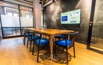 Modernes Büro in der Münchner Altstadt am Viktualienmarkt 8, ideal für Meetings. Die Bürofläche verfügt über einen Holztisch und schwarze Stühle mit blauen Kissen.