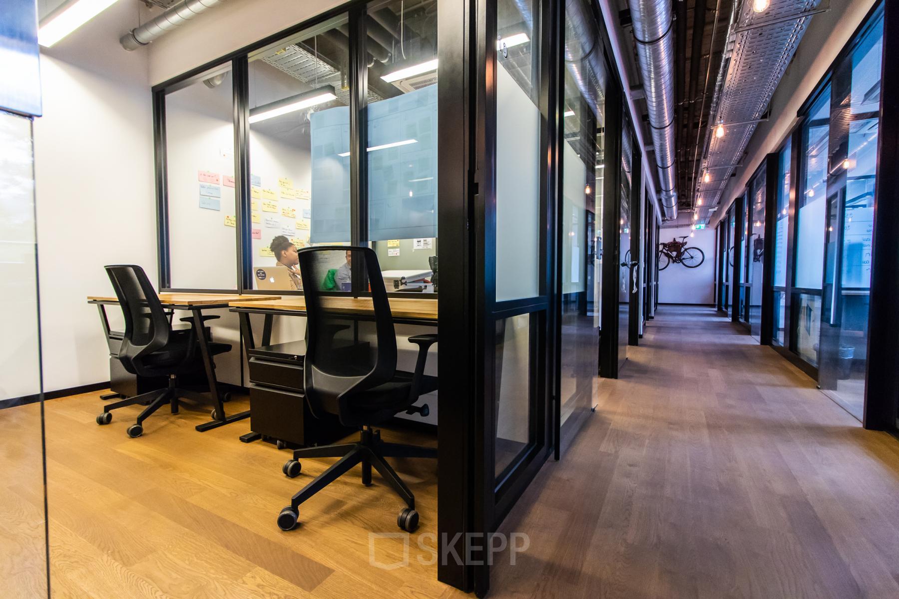 Modernes Büro im Viktualienmarkt 8, München Altstadt mit Glaswänden und ergonomischen Stühlen. Ideal, um Büroraum zu mieten. Eine Person arbeitet konzentriert am Schreibtisch.