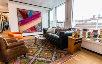 Stylish office lounge at Herzogspitalstraße 24, Munich Old Town, featuring modern seating, vibrant artwork, and a scenic view. Ideal for those seeking office space rental.