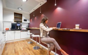Moderne Kaffee-Ecke im Büro an der Maximilianstraße 2, München Altstadt mit einer Frau, die an einem Laptop arbeitet.