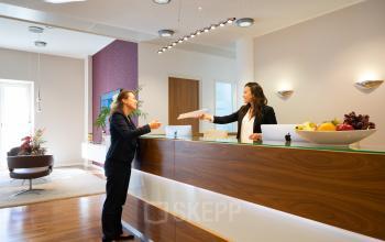 Repräsentatives Büro in der Maximilianstraße 2, München Altstadt, mit Empfangsbereich, an dem zwei Personen geschäftliche Unterlagen austauschen.