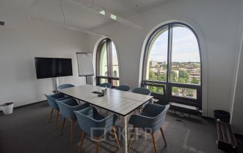 Conference room at Christoph-Rapparini-Bogen 25, Munich Laim, featuring a large table, blue chairs, a TV, and big arched windows with natural light.