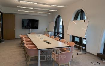 Conference room at Christoph-Rapparini-Bogen 25 in Munich Laim with a large table, pink chairs, whiteboards, and a screen.