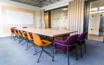 Moderne, helle büroraum mieten im München Maxvorstadt mit großem Konferenztisch, zwölf farbigen Stühlen und Glaswänden, ideal für Teammeetings.