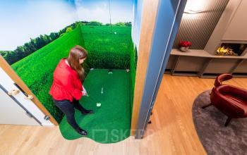 Büro in Hopfenstraße 8, München Maxvorstadt: Ein kreativ gestalteter Raum mit Indoor-Minigolf-Ecke. Eine Person spielt Minigolf, während im Hintergrund moderne Einrichtung sichtbar ist. Ideal, um büroraum zu mieten.