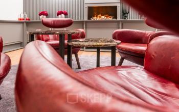 Gemütlicher Büroraum in der Hopfenstraße 8, München Maxvorstadt, mit roten Ledersesseln und dekorativem Kamin. Büroraum mieten für kreative Pausen in eleganter Atmosphäre.