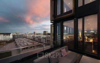 Aussicht von einem Balkon der Luise-Ullrich-Straße 14 auf das Stadtbild von München Neuhausen bei Sonnenuntergang. Das Foto zeigt moderne Büroflächen in einem gläsernen Hochhaus.