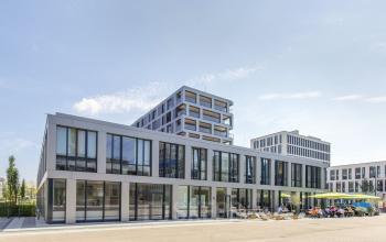 Modernes Bürogebäude in der Arnulfstraße 122-126, München Neuhausen. Große Fensterfassade, Außensitzbereich mit Menschen bei geschäftlichen Gesprächen.
