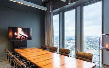 Konferenzraum mit Holztisch und Ledersesseln in der Mies-van-der-Rohe-Straße 8, München Schwabing, mit Blick auf die Stadt durch große Fenster.