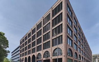 Bürogebäude in der Mühldorgstraße 8 im München Werksviertel, ideal für Bürofläche mieten. Moderne Architektur mit Backsteinfassade und großen Fenstern. Autos und Menschen sind auf der Straße zu sehen.