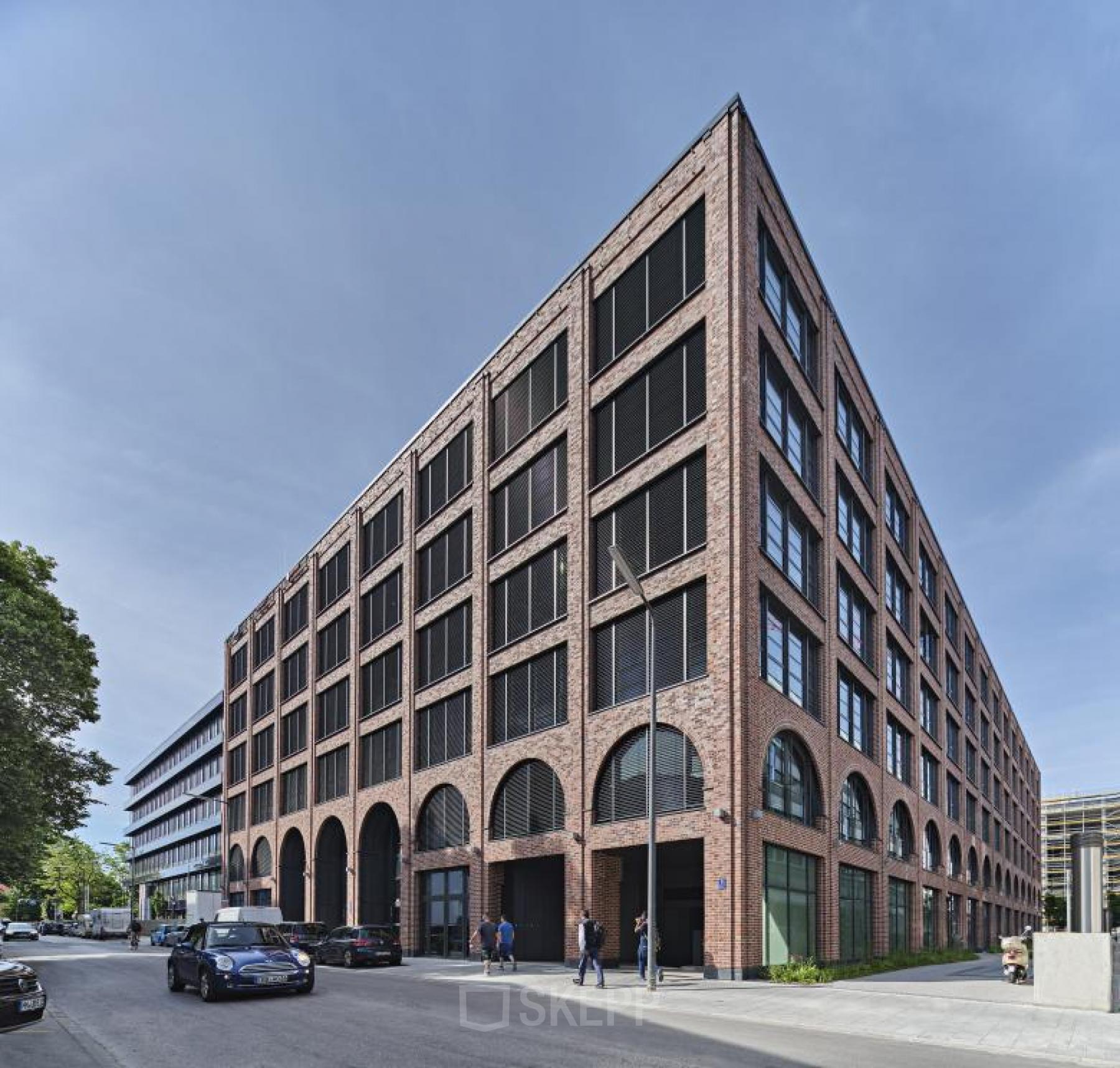 Bürogebäude in der Mühldorgstraße 8 im München Werksviertel, ideal für Bürofläche mieten. Moderne Architektur mit Backsteinfassade und großen Fenstern. Autos und Menschen sind auf der Straße zu sehen.