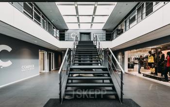 Interior view of an office building at Rijksweg 79, Naarden, featuring a central staircase, modern design elements, large skylight, and adjacent workspaces. Ideal office space rental option.