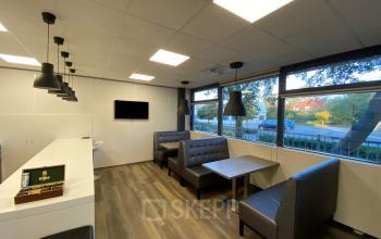 Modern lounge area at the office located at Rijksweg 79, Naarden. The space is furnished with comfortable seating, tables, and a wall-mounted TV.