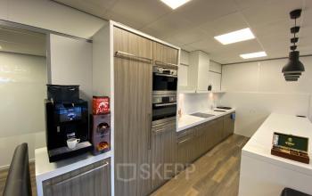 Modern kitchen area in an office space at Rijksweg 79, Naarden, featuring cabinets, built-in oven, coffee machine, and snack dispenser.