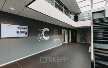 Office space at Rijksweg 79, Naarden featuring a reception area with modern design, large screen, and staircase to the upper floor.