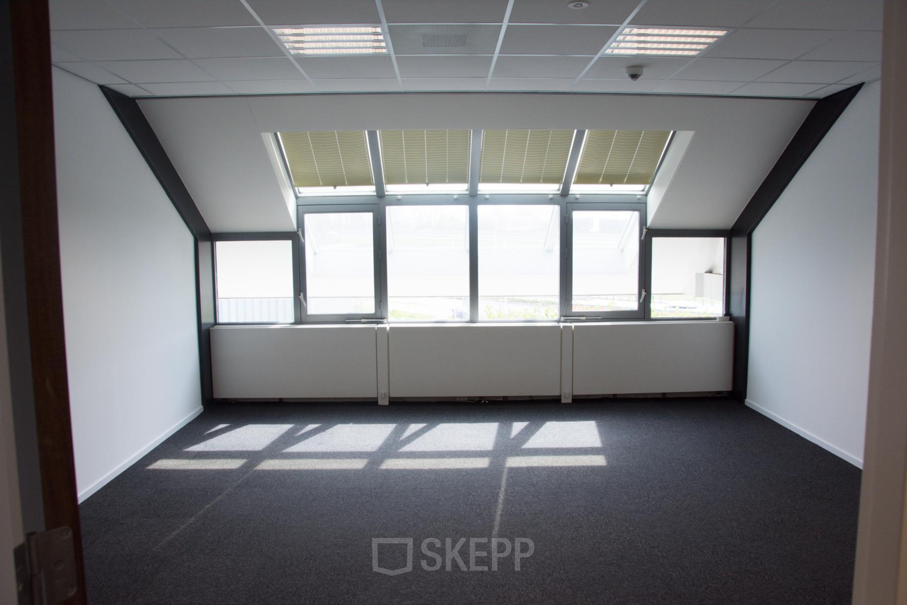 Empty office space with carpet flooring, large windows, and ceiling lights at Rijksweg 79, Naarden, available for office space rental.