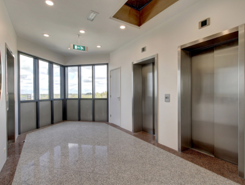 Bright, modern hallway space with elevators at Nevelgaarde 8-35, Nieuwegein, perfect for businesses seeking office space rental. Large windows offer a view of the exterior surroundings.