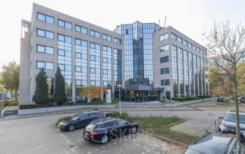 Exterior view of office building at Nevelgaarde 8-19, Nieuwegein, featuring modern glass façade and ample parking. Ideal location for office space rental.