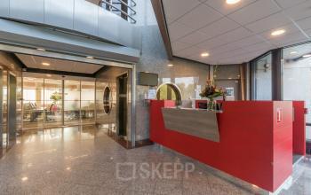 Bright and modern interior at Nevelgaarde 8-19, Nieuwegein, featuring a spacious reception area with sleek red desk, perfect for office space rental. Glass doors enhance the professional ambiance.