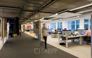 Modern office space rental at Zoomstede 13-25, Nieuwegein, featuring an open floorplan with workstations, a punching bag, and people working at desks.