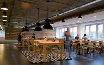 Modern office space rental at Zoomstede 13-25, Nieuwegein featuring wooden tables, pendant lighting, large windows, and professionals working or conversing.