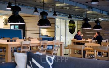 Modern workspace at Zoomstede 13-25, Nieuwegein featuring wooden tables, chairs, and pendant lighting with two individuals engaged in a business discussion.