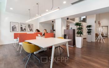 Modern office workspace at Oranjesingel 51 in Nijmegen featuring sleek, minimalist design with collaborative desks and vibrant chairs. Bright lighting and contemporary artwork enhance the inviting atmosphere. Ideal for office space rental.