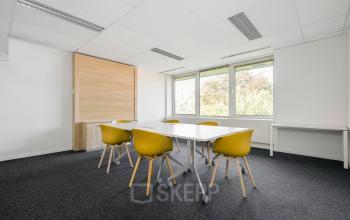 Bright office space for rent at Oranjesingel 51, Nijmegen, featuring a minimalist meeting room with yellow chairs and large windows offering abundant natural light.