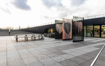 Exterior view of an office space at Jonkerbosplein 52, Nijmegen, showcasing a modern design with ample outdoor seating. Ideal for those looking to rent office space.