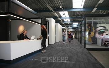 Modern office space rental at Koopvaardijweg 2, Oosterhout Nb with employees engaging in business activities at reception and in walkway.