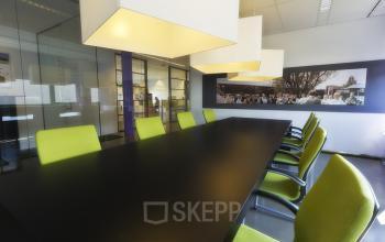 Sleek office space rental at Koopvaardijweg 2, Oosterhout Nb with vibrant green chairs around a long dark table and modern lighting fixtures.