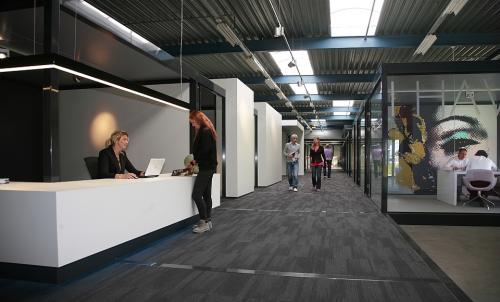 Modern office space rental at Koopvaardijweg 2, Oosterhout Nb with employees engaging in business activities at reception and in walkway.