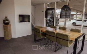 A furnished office space at Abdis van Thornstraat 74 in Oosterhout Nb, featuring a meeting table with chairs, a wall-mounted TV, and decorative lighting. Ideal for those looking to rent office space.